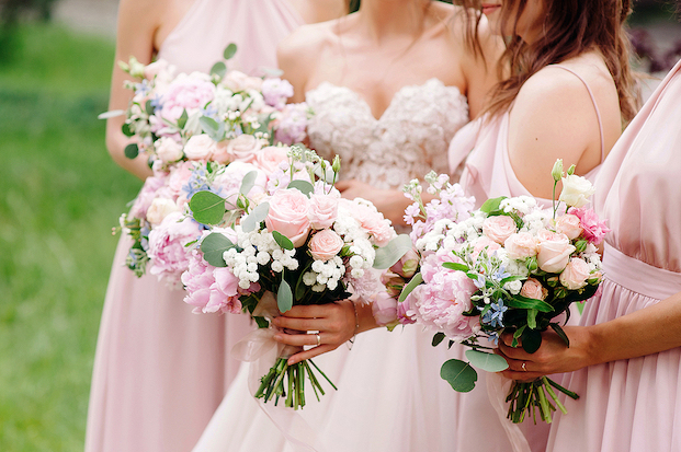 Closeup view of the hands of three bridesmaids in pink holding pink and white floral bouquets.